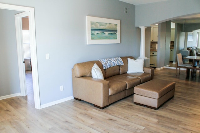 living room featuring arched walkways, light wood-style flooring, baseboards, and ornate columns