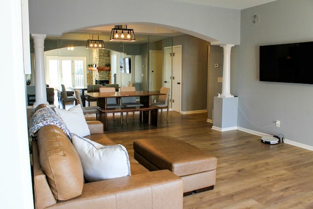 living room featuring wood finished floors, arched walkways, a stone fireplace, baseboards, and ornate columns