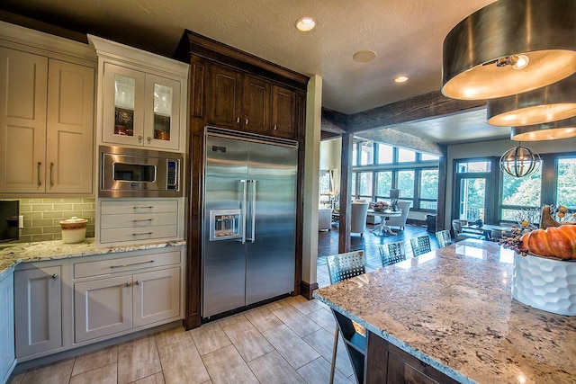 kitchen featuring light stone counters, backsplash, a textured ceiling, built in appliances, and beamed ceiling