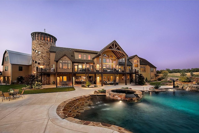 back of property at dusk featuring a balcony, metal roof, a yard, a patio area, and a pool with connected hot tub