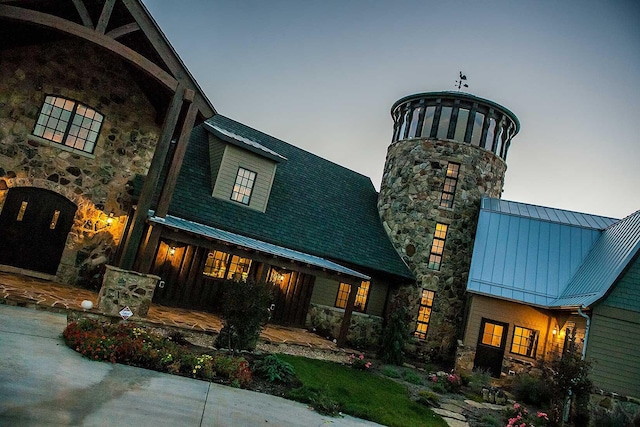 rear view of house featuring stone siding, a chimney, metal roof, and a standing seam roof