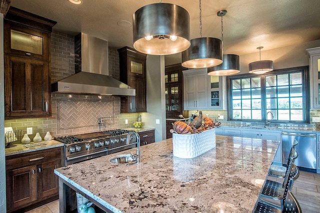 kitchen featuring wall chimney range hood, backsplash, stainless steel appliances, and a sink