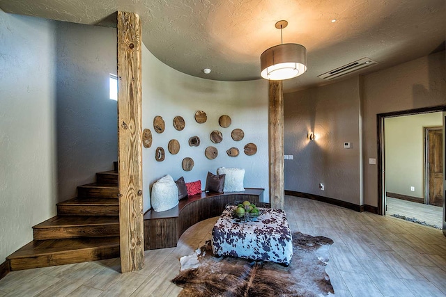 interior space featuring a textured ceiling, wood finished floors, visible vents, baseboards, and stairway