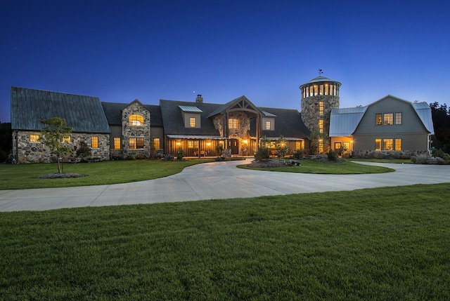 view of front of property featuring curved driveway, a gambrel roof, a front yard, metal roof, and stone siding