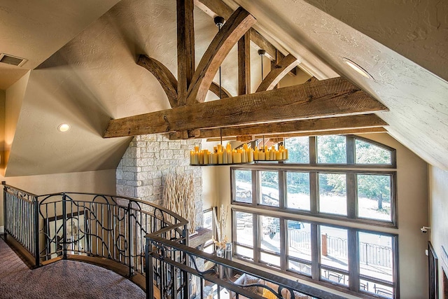 interior space featuring lofted ceiling with beams, visible vents, and a textured wall