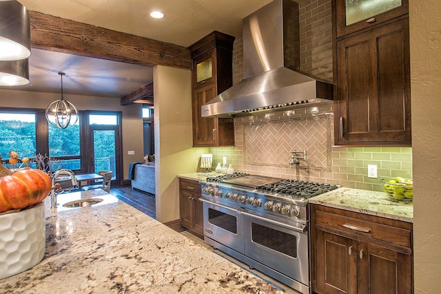 kitchen with range with two ovens, a sink, wall chimney exhaust hood, and tasteful backsplash