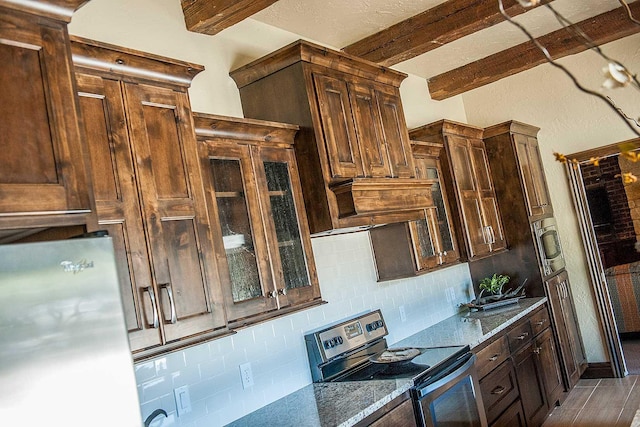 kitchen with appliances with stainless steel finishes, beamed ceiling, dark stone countertops, and tasteful backsplash