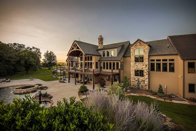 back of property with a fire pit, stone siding, a lawn, a chimney, and a patio area