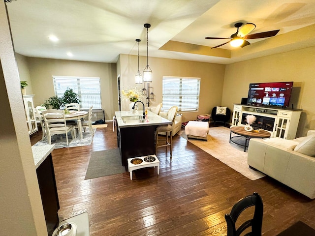 living room featuring a tray ceiling, dark wood-style flooring, a fireplace, a ceiling fan, and baseboards