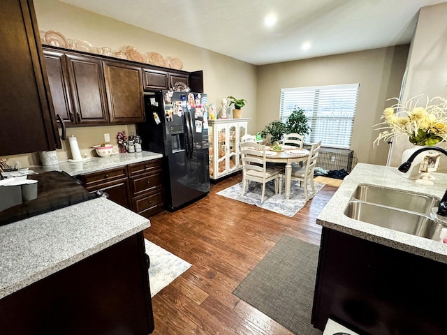 kitchen featuring dark wood finished floors, dark brown cabinetry, black refrigerator with ice dispenser, and a sink