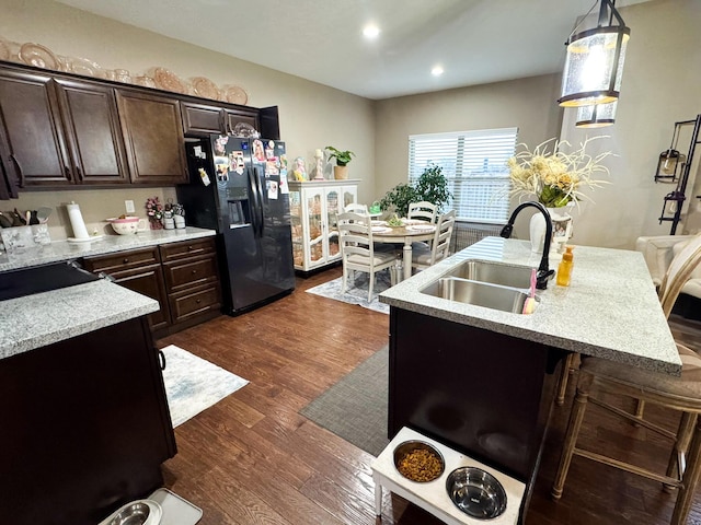 kitchen featuring dark wood finished floors, light countertops, a sink, dark brown cabinetry, and black fridge