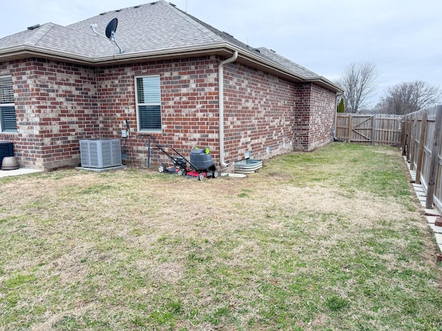 view of property exterior with brick siding, a shingled roof, a lawn, central AC unit, and a fenced backyard