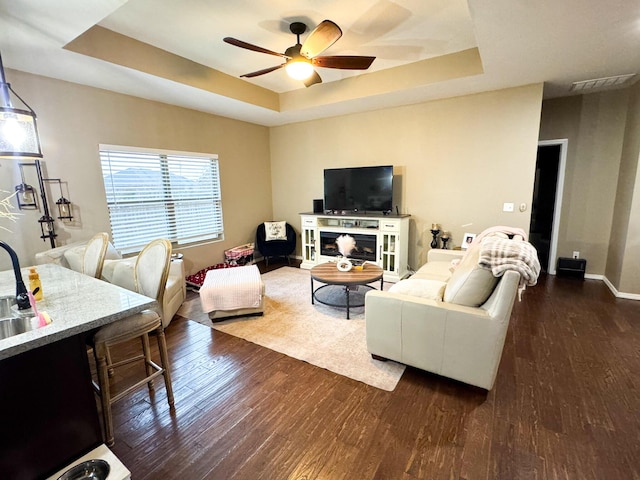 living area with visible vents, baseboards, dark wood finished floors, a ceiling fan, and a raised ceiling