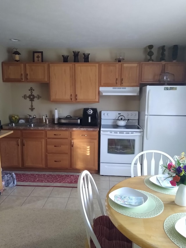 kitchen featuring light tile patterned floors, under cabinet range hood, white appliances, a sink, and dark countertops