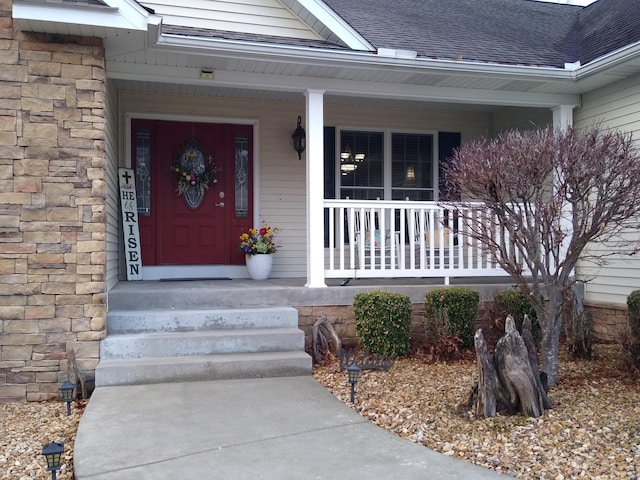 doorway to property with stone siding, a shingled roof, and a porch