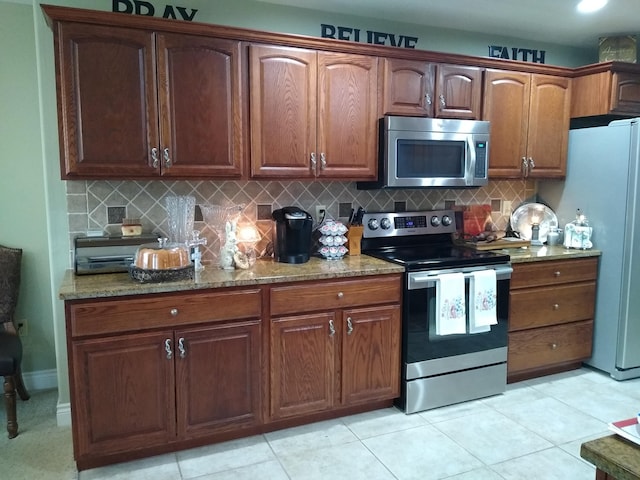 kitchen with stainless steel appliances, light tile patterned flooring, light stone counters, and tasteful backsplash