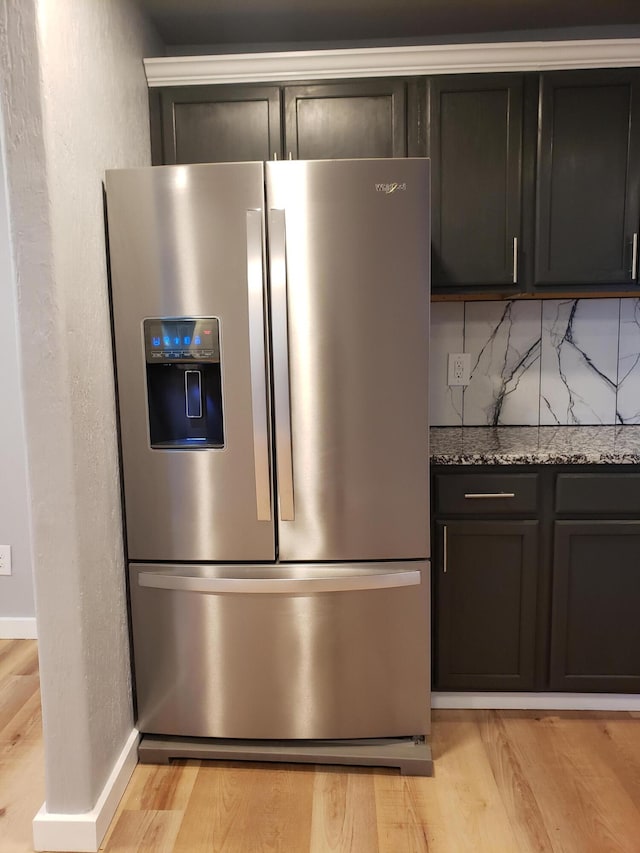 kitchen with light wood-type flooring, stainless steel fridge with ice dispenser, and light stone countertops