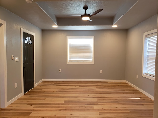 entrance foyer with a ceiling fan, light wood-type flooring, a tray ceiling, and baseboards