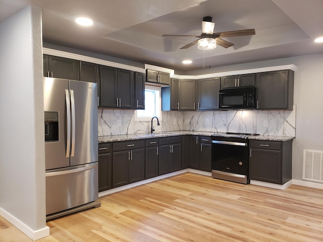 kitchen with a raised ceiling, visible vents, light wood-style floors, black microwave, and stainless steel fridge