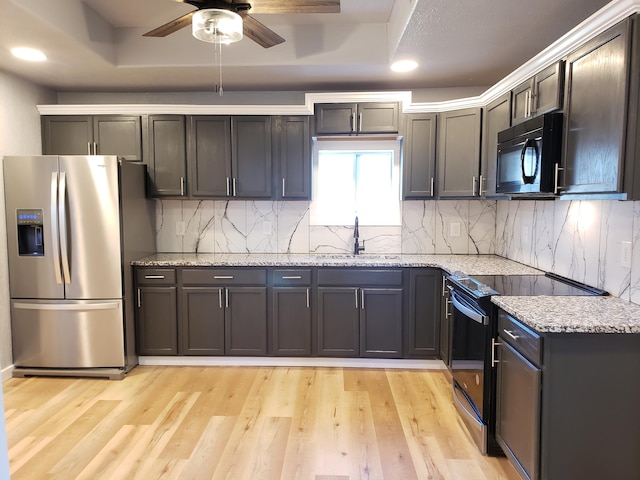 kitchen featuring black appliances, light wood-style floors, a raised ceiling, and a sink