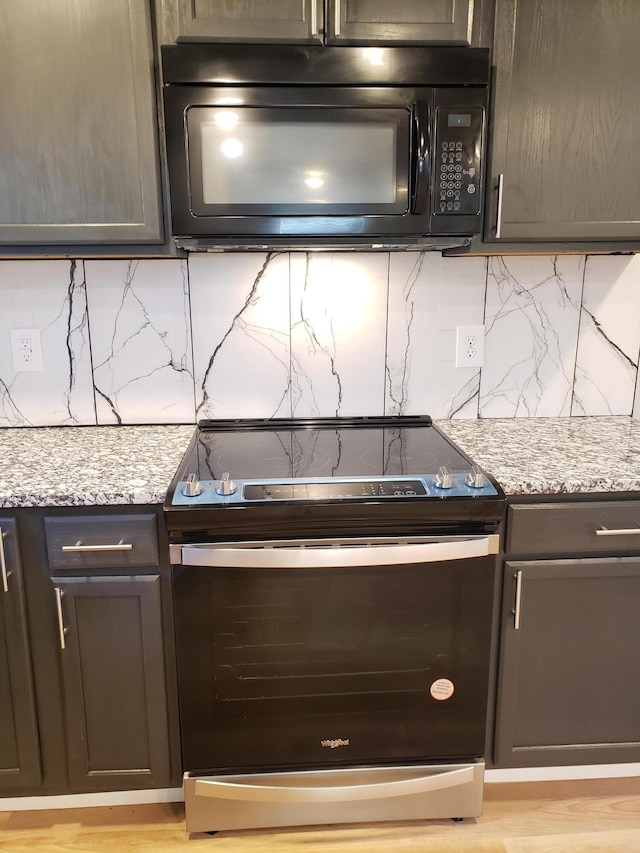 kitchen featuring stainless steel range with electric stovetop, black microwave, decorative backsplash, and light stone counters