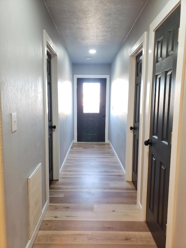 doorway with a textured ceiling, light wood finished floors, visible vents, and baseboards