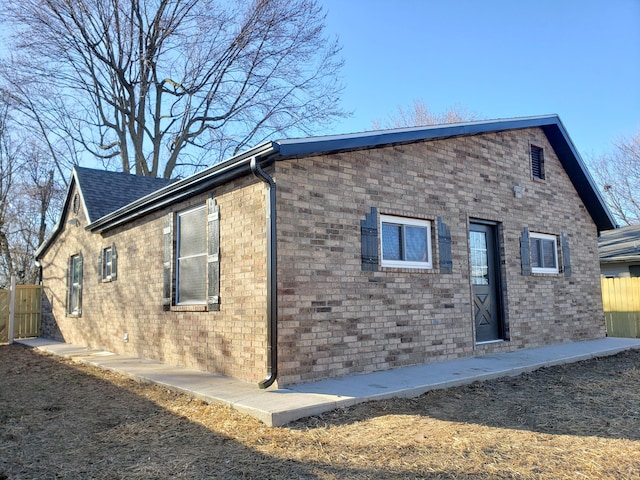 view of side of home with a shingled roof, brick siding, and fence