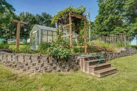 view of play area with an outbuilding, a vegetable garden, a lawn, and a greenhouse