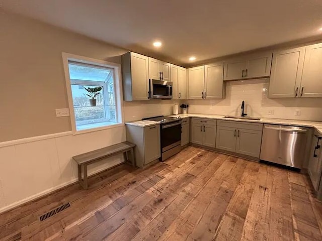 kitchen with gray cabinetry, a sink, visible vents, light wood-style floors, and appliances with stainless steel finishes