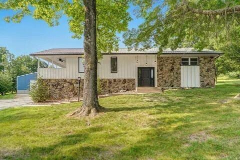 exterior space featuring stone siding, ceiling fan, and a front lawn