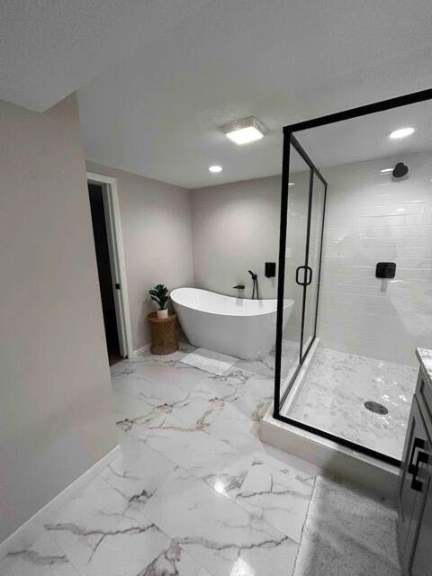 full bathroom featuring a stall shower, marble finish floor, a freestanding bath, and baseboards