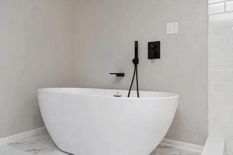 full bathroom with marble finish floor, a freestanding tub, and baseboards