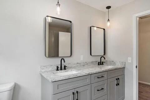 full bathroom with toilet, double vanity, baseboards, and a sink