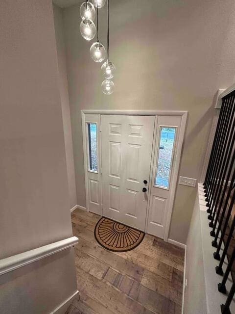 entryway with a wealth of natural light, baseboards, a towering ceiling, and hardwood / wood-style floors