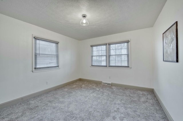 empty room with a textured ceiling, carpet floors, visible vents, and baseboards