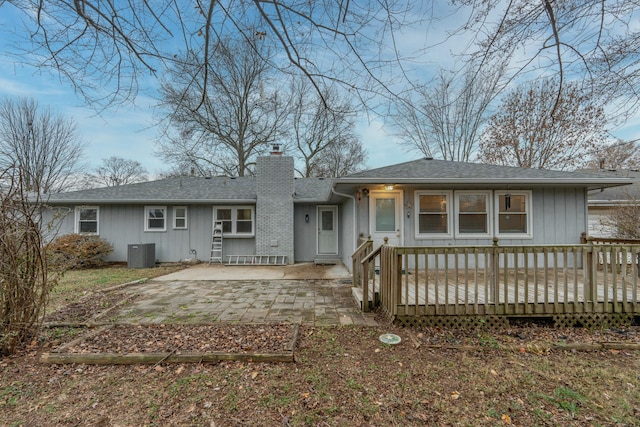 view of front of property with central AC, roof with shingles, a wooden deck, a chimney, and a patio area