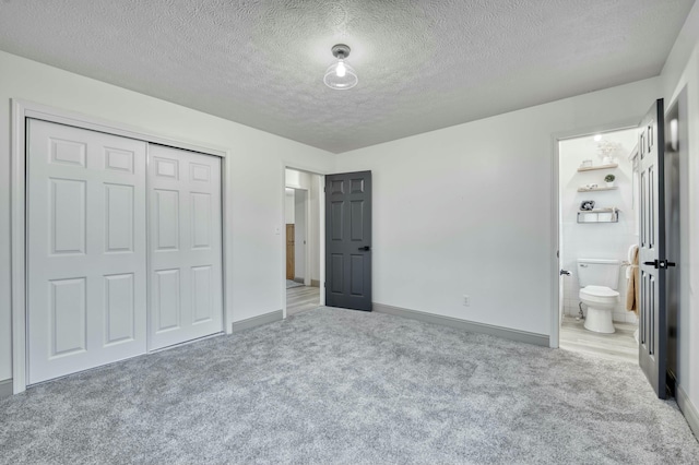 unfurnished bedroom with a closet, carpet flooring, a textured ceiling, and ensuite bath