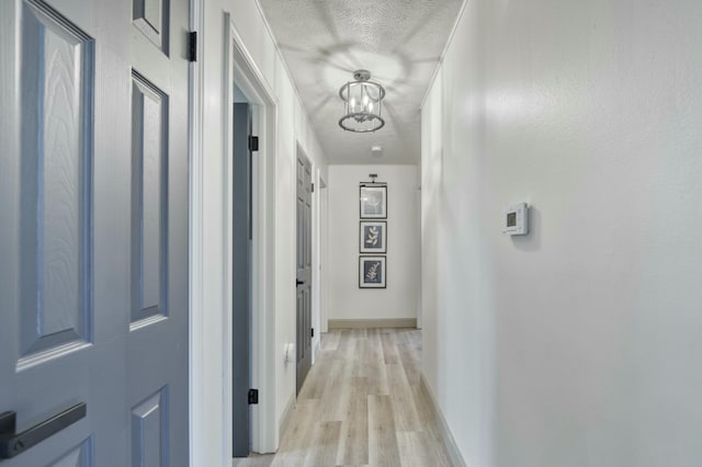 hall featuring a chandelier, baseboards, a textured ceiling, and light wood finished floors