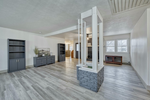 living area with a textured ceiling, ceiling fan, light wood-style flooring, a fireplace, and baseboards