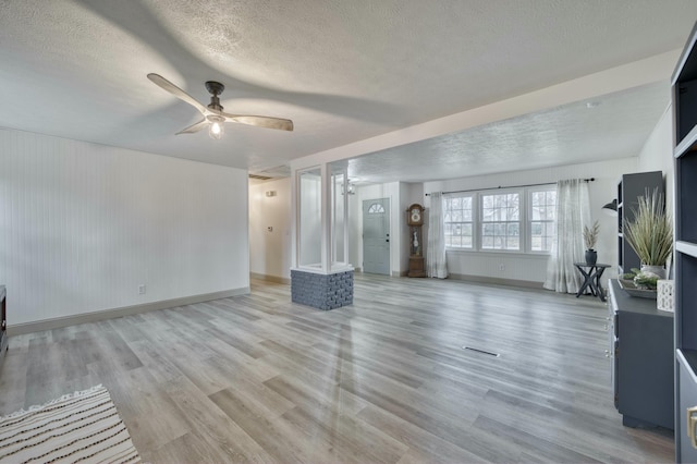 unfurnished living room featuring visible vents, ceiling fan, a textured ceiling, light wood-type flooring, and baseboards