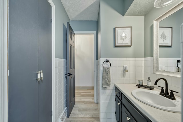 bathroom with tile walls, a textured ceiling, vanity, and wood finished floors