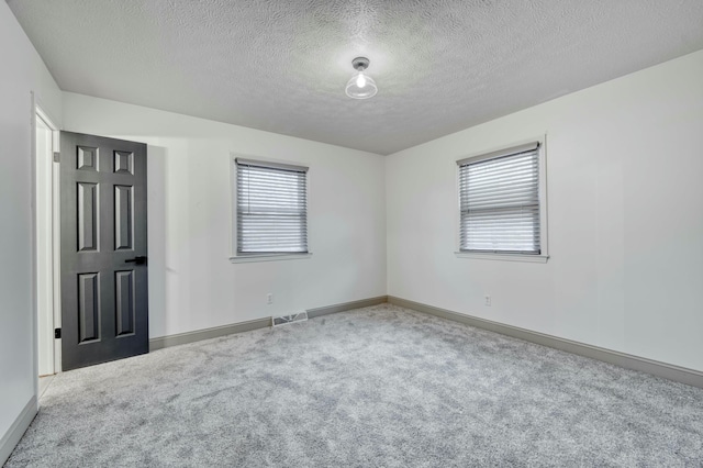 empty room with a healthy amount of sunlight, carpet, visible vents, and a textured ceiling