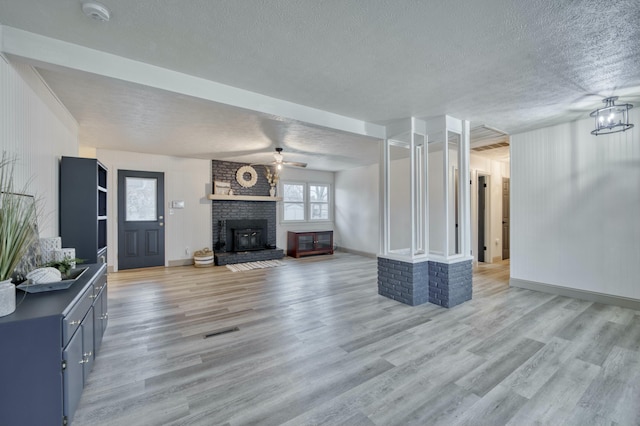 living room with visible vents, light wood-style floors, a ceiling fan, a brick fireplace, and a textured ceiling