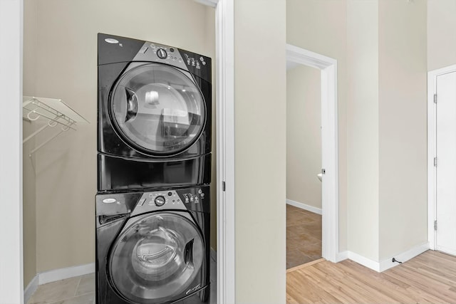 laundry room featuring stacked washer and dryer, wood finished floors, laundry area, and baseboards