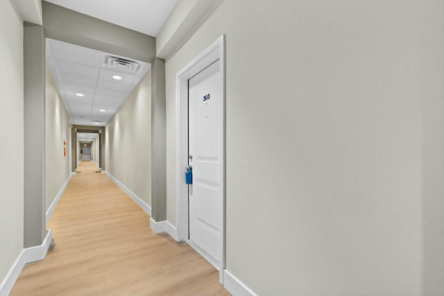 hall featuring a paneled ceiling, visible vents, light wood-style flooring, and baseboards