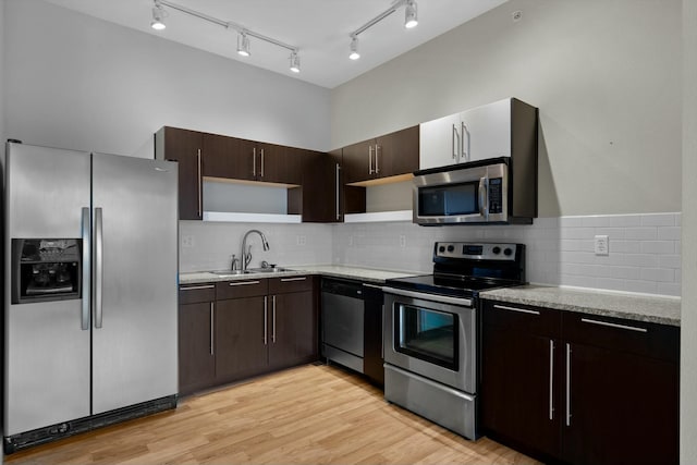 kitchen featuring light wood-style flooring, dark brown cabinetry, a sink, appliances with stainless steel finishes, and open shelves