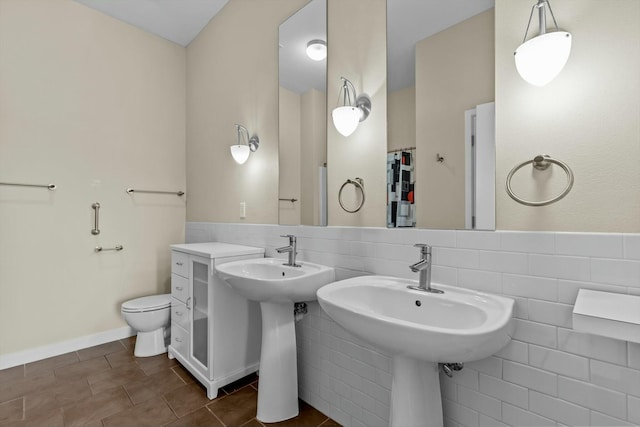 bathroom featuring baseboards, tile walls, and toilet