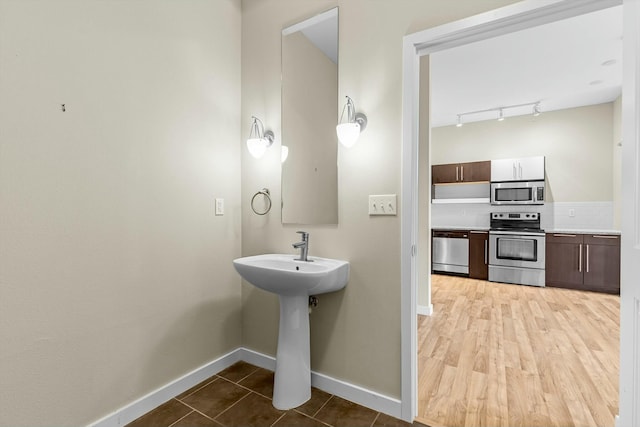 bathroom featuring a sink, wood finished floors, baseboards, backsplash, and track lighting