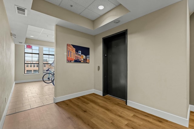 hall with a paneled ceiling, elevator, visible vents, and wood finished floors