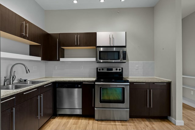 kitchen with light wood finished floors, open shelves, stainless steel appliances, light countertops, and a sink